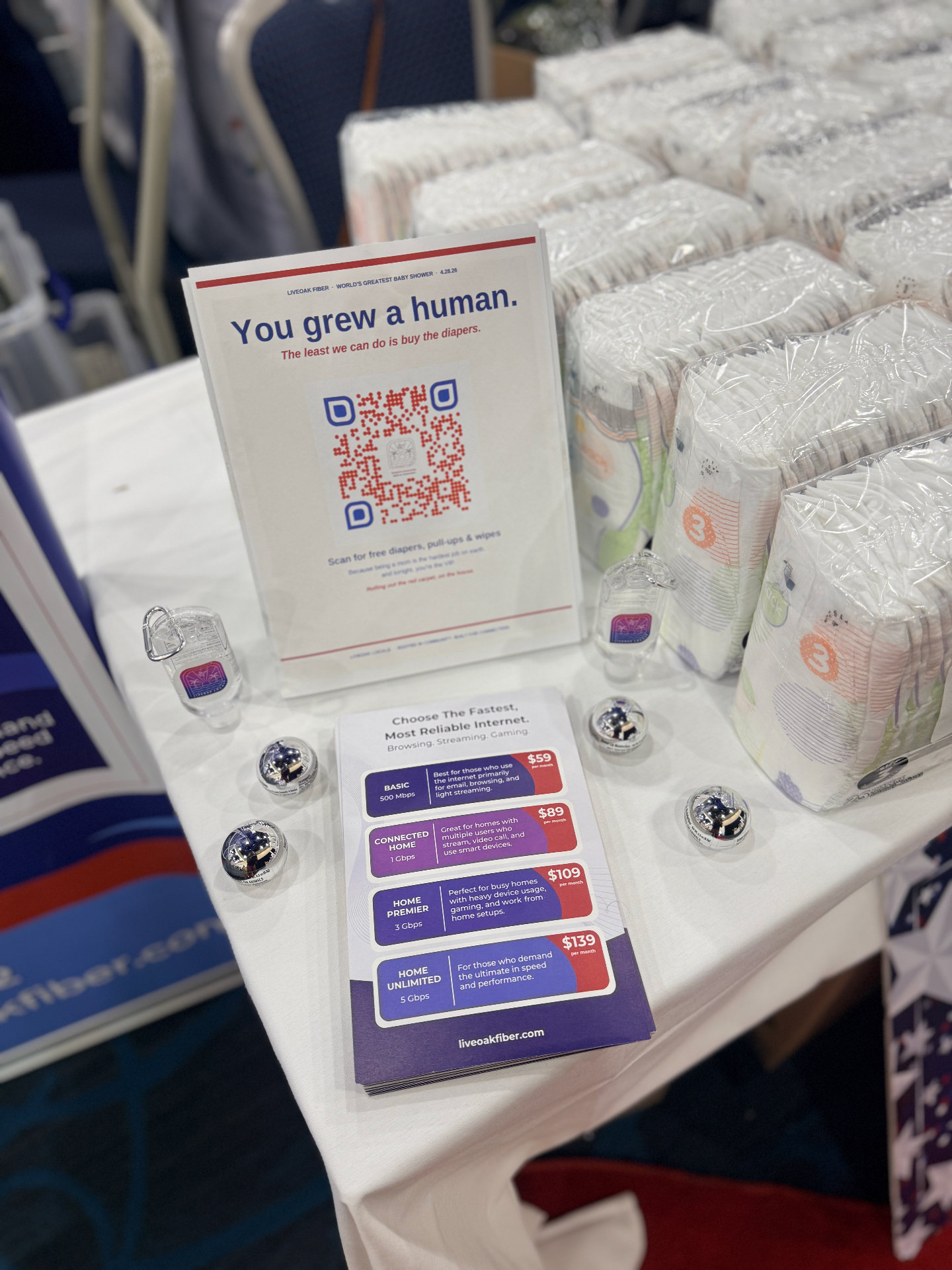 A "You grew a human, the least we can do is buy the diapers" sign beside stacked diapers at a military family event, featured in a PCS diaper checklist for military families.