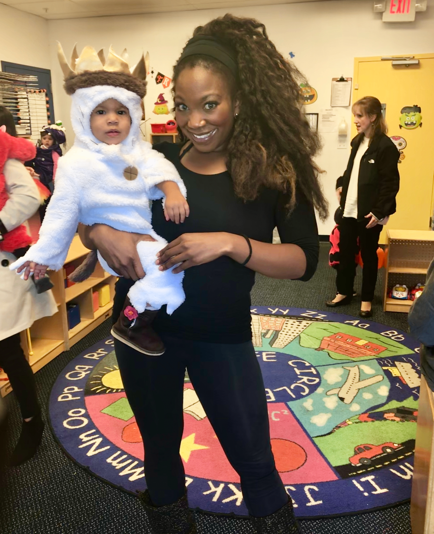 A mother holding her young child in a daycare classroom, featured in a guide to handling potty-training accidents at daycare.