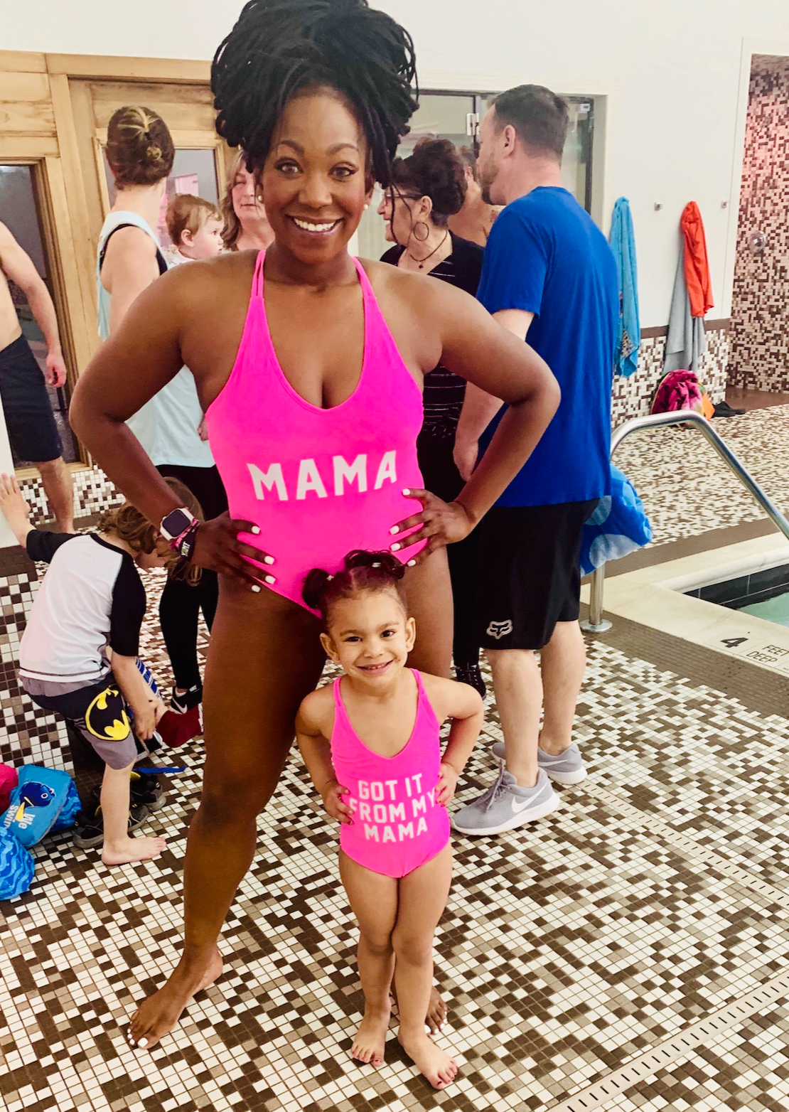 A mother holding her young child in swimsuits at an indoor pool, featured in a guide to swim diapers.