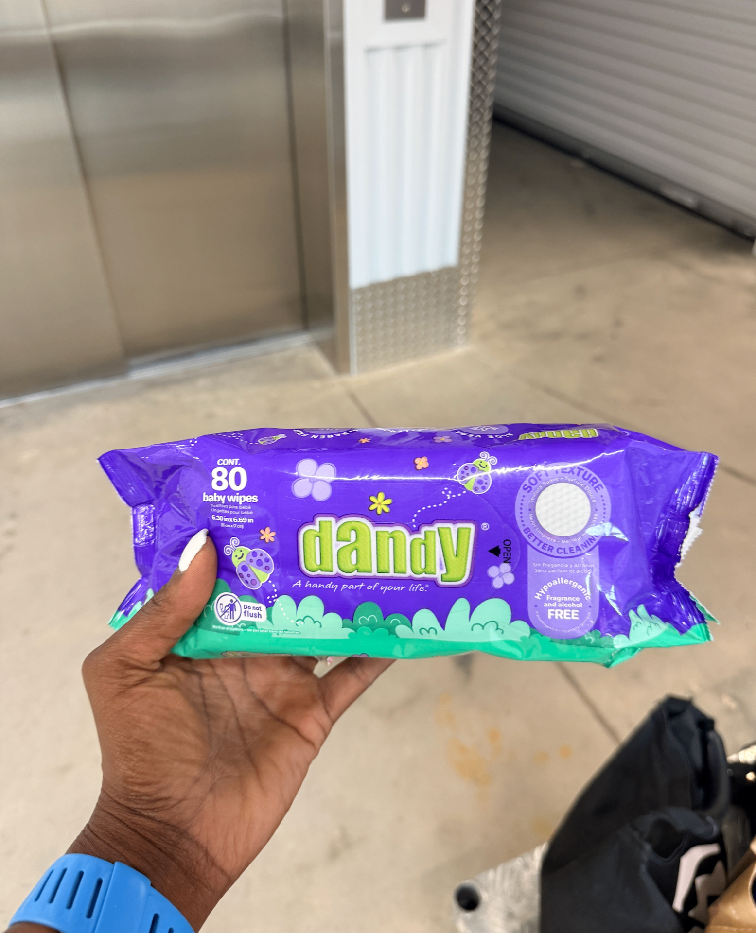 A hand holding an unopened pack of baby wipes near a storage elevator