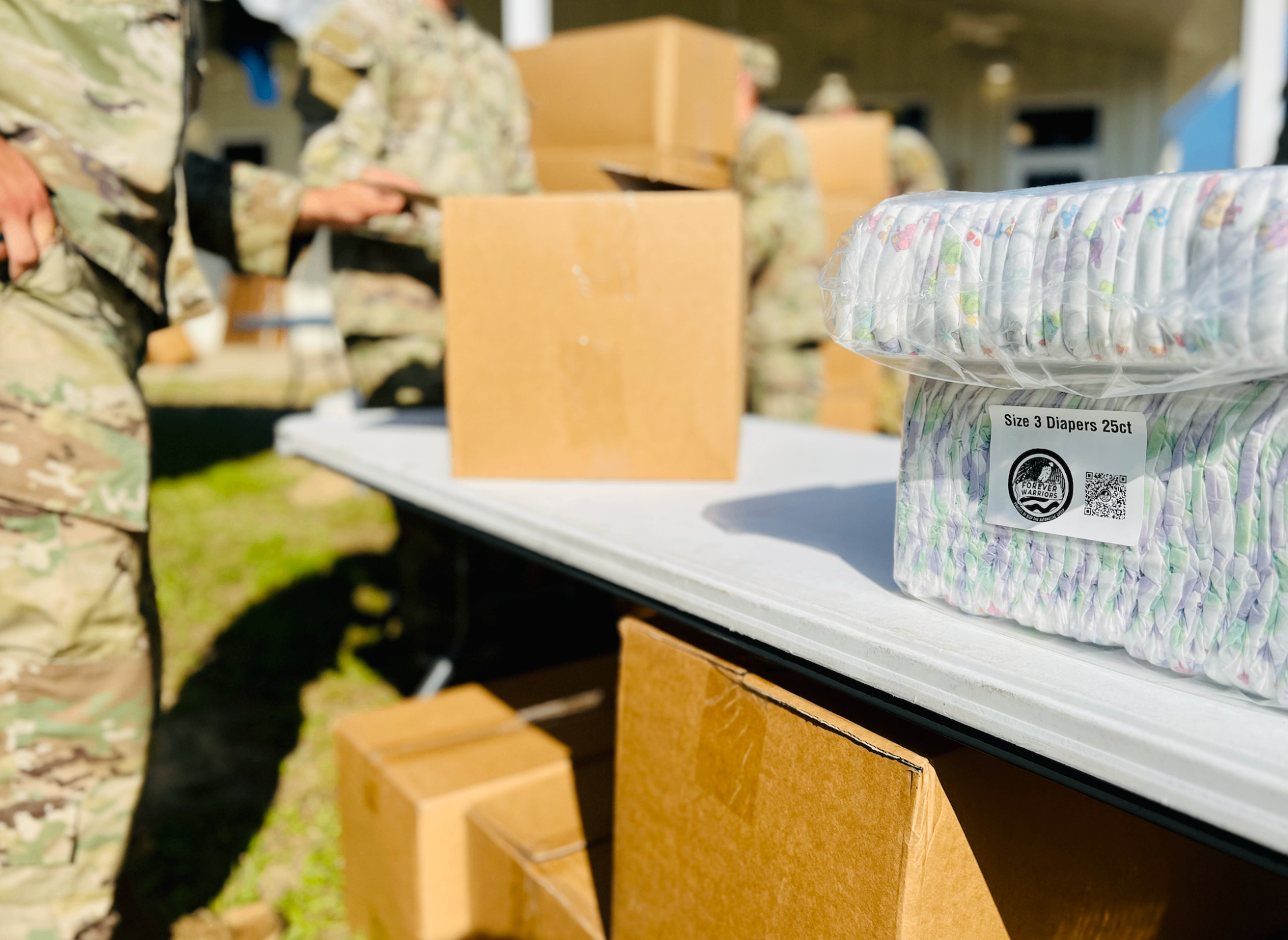 Packaged diapers on a table at a military diaper distribution with service members in the background, featured in a guide to diaper assistance for military families.